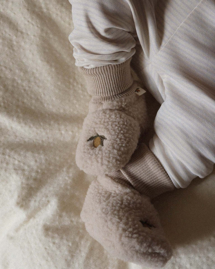 A baby wearing a light striped onesie with an organic cotton lining and soft safa boots in oxford tan by konges sløjd, featuring small embroidered designs, lying on a cream-colored blanket.