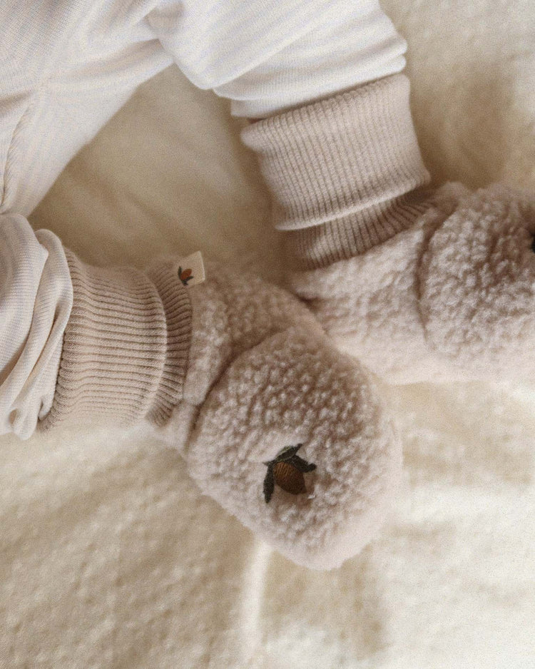 Close-up of a baby wearing konges sløjd safa boots in oxford tan, featuring soft, fluffy fleece with a small embroidered peach design and an organic cotton lining, lying on a textured cream blanket.