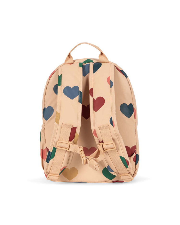 Introducing the rainy backpack in bon coeur coloré by konges sløjd—a peach-hued kids’ adventure backpack adorned with vibrant red, blue, and green heart patterns. Shown from the back against a white background, it features adjustable straps and a top handle for convenience. Lightweight and stylish, it’s perfect for little explorers on the go.