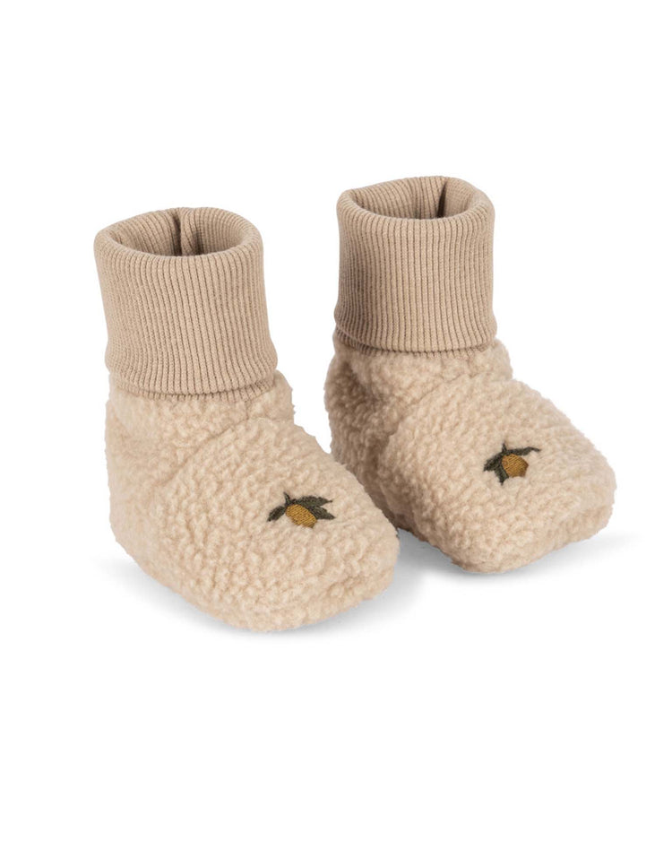 A pair of safa boots in oxford tan by konges sløjd, featuring beige fleece with ribbed ankle cuffs and small yellow embroidered lemons on top, crafted with an organic cotton lining for extra softness, shown on a white background.