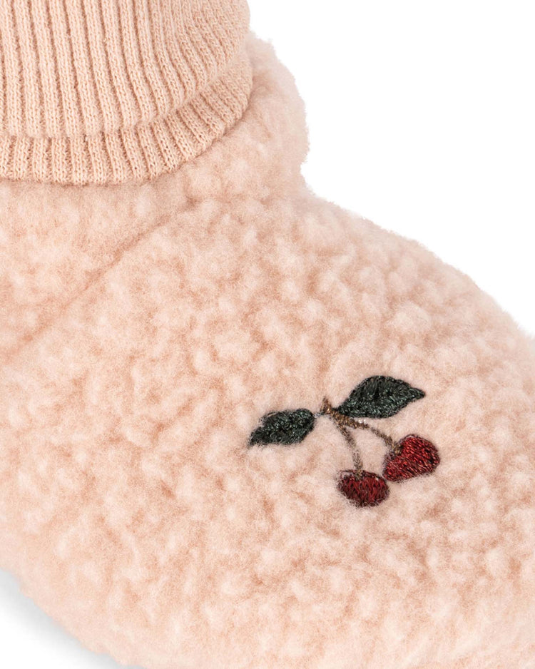 A close-up of the konges sløjd safa boots in rose smoke—a soft, pink fleece slipper adorned with cherry and leaf embroidery. The slipper is lined with organic cotton for added comfort, while a ribbed pink sock peeks out above.