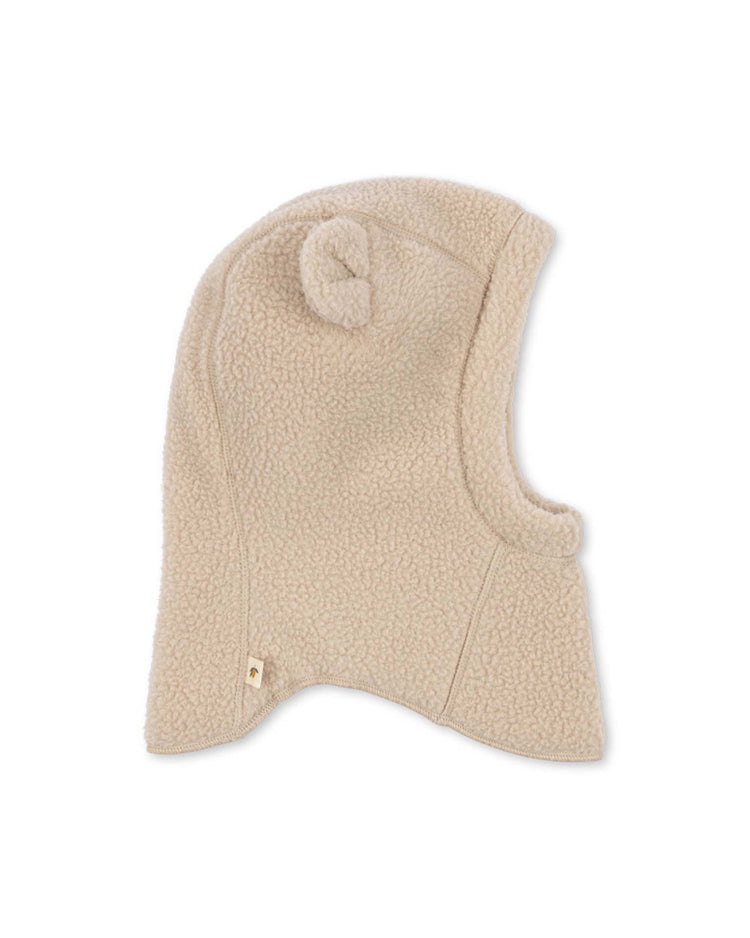 A safa helmet in oxford tan by konges sløjd, featuring a rounded top and a small fabric knot detail, designed to cover the head, ears, and neck (KS105768), is displayed on a white background.