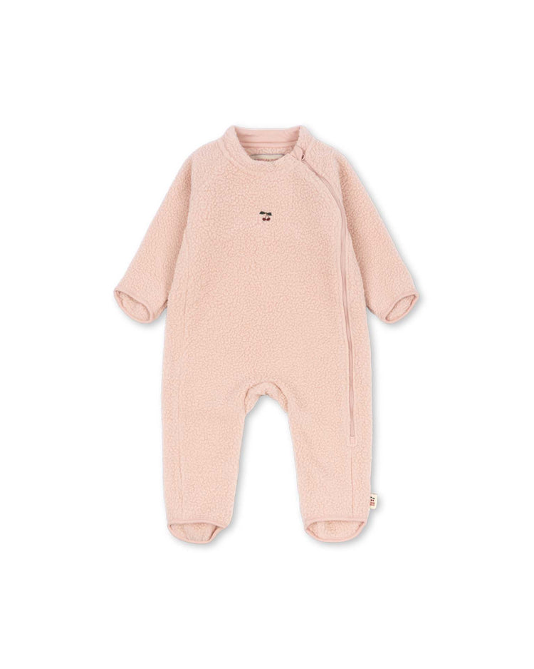 The safa onesie in rose smoke by konges sløjd is a light pink baby fleece outfit with long sleeves and legs, crafted from soft recycled polyester fleece. It features foldable cuffs for adjustable comfort, a small embroidered face on the chest, and a diagonal zipper running from the neckline to the left leg. The onesie is displayed laid flat against a white background.