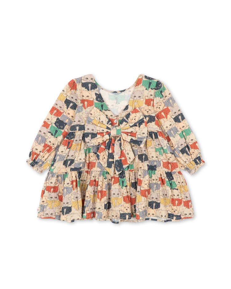 The elin long sleeve bow dress in like cats and dogs by konges sløjd is a knee-length children's dress crafted from organic cotton, featuring voluminous long sleeves, a round neckline, a gathered skirt, and a multicolored cat print with a large bow on the front.