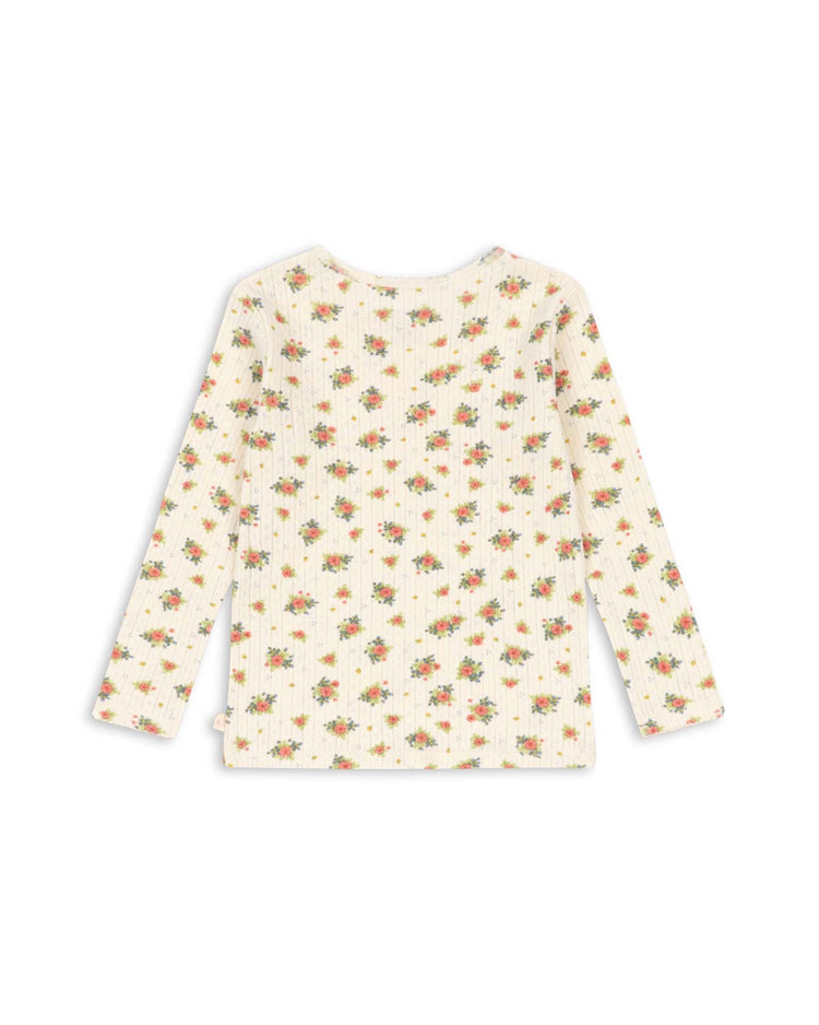 The minnie blouse in rosetto by konges sløjd is a long-sleeve, cream-colored organic cotton shirt with a ribbed texture and an all-over small floral pattern in red, yellow, and green. This GOTS certified blouse is shown laid flat with the back side facing up.