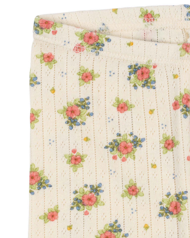 The minnie pants in rosetto by konges sløjd feature a cream-colored ribbed fabric with a textured pointelle pattern, adorned with small red, blue, and green floral designs scattered throughout—perfect for cozy everyday leggings.