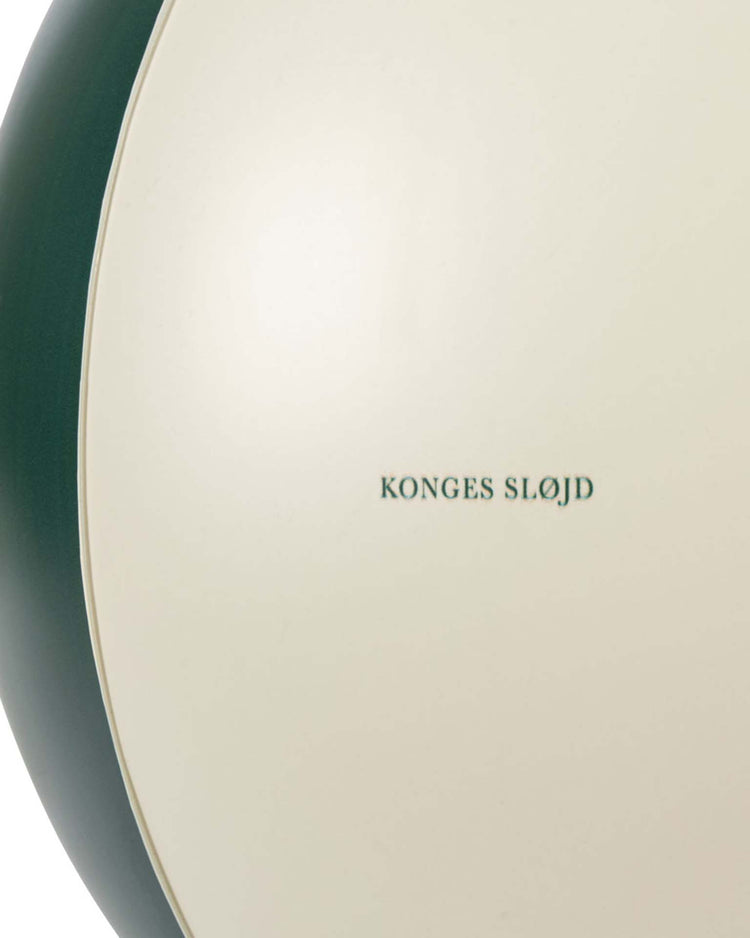 Close-up of the "beach ball in green stripe" by konges sløjd, featuring a cream surface with dark green stripes and the brand's name. This stylish pool toy is perfect for summer fun.