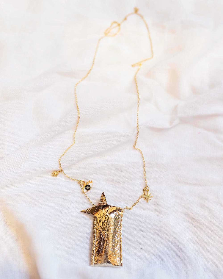 Gold handmade amulet crystal necklace in distress platinum on a white fabric surface by atsuyo et akiko.