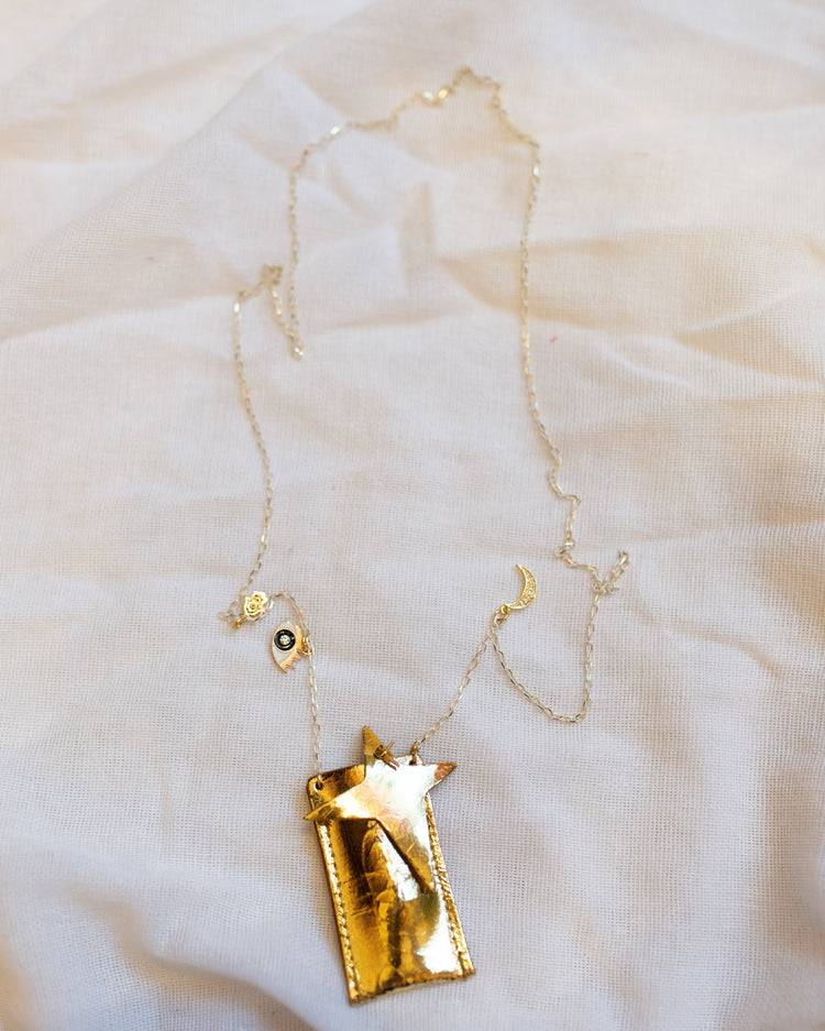 A handmade amulet crystal necklace in foil gold with charms by atsuyo et akiko on a white fabric surface.