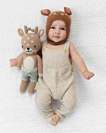 Baby Elliott dressed in a knitted outfit lying next to a Cuddle + Kind "Elliott the Fawn" toy.