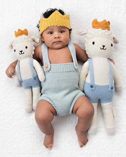 Baby Sebastian, the little prince wearing a knitted crown hat, flanked by two cuddle + kind sebastian the lamb stuffed animals in matching outfits.