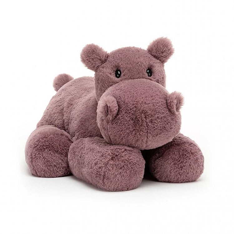 A large Jellycat Huggady Hippo stuffed animal is laying down on a white background.