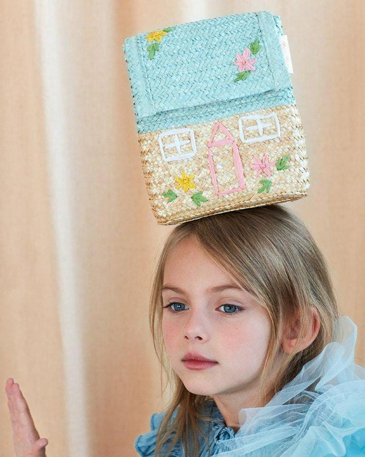 A child balancing a small, meri meri straw bag on her head.