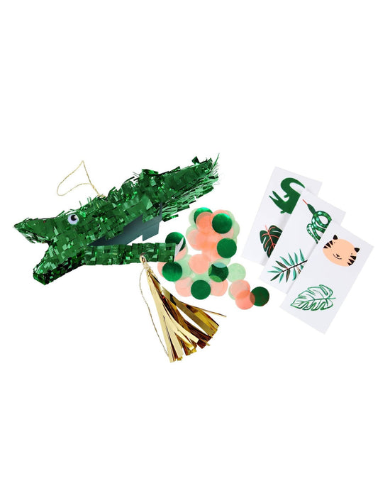 A green crocodile piñata favor resembling a croc, coupled with decorative cards and tassels, isolated on a white background. (Brand Name: meri meri)