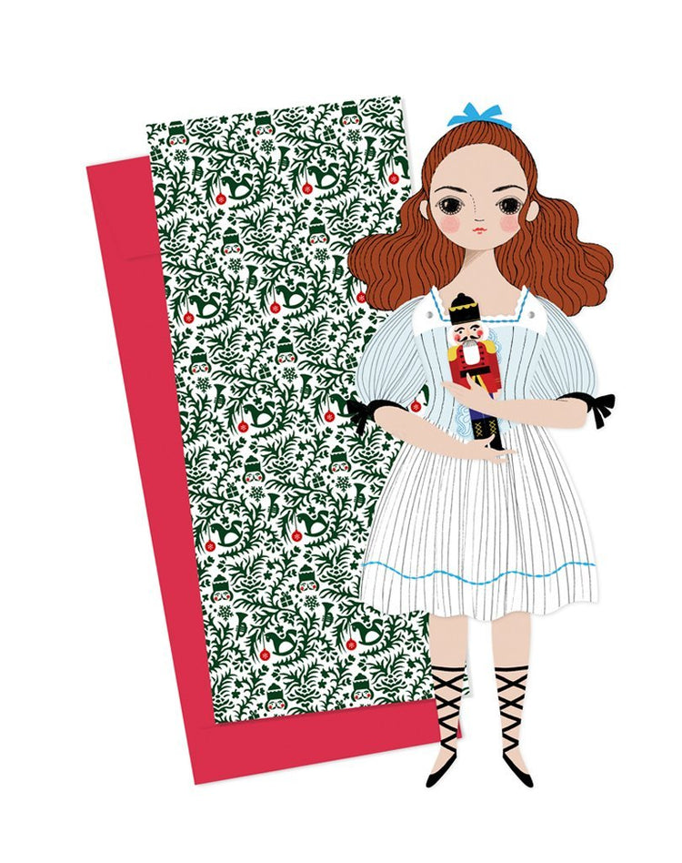 Illustration of a girl with red hair holding a Clara Mailable Paper Doll from Of Unusual Kind, standing next to a floral-patterned panel with a red border.