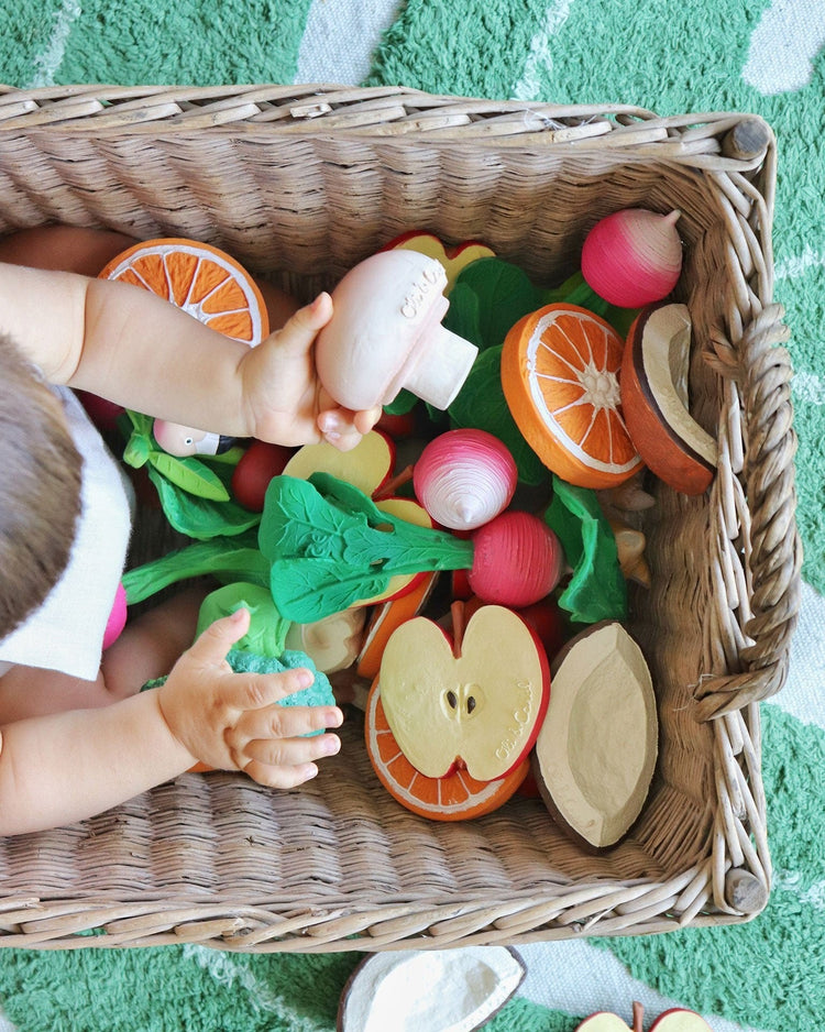 A baby playing with Oli + Carol's Manolo the Mushroom natural rubber toy in a wicker basket.