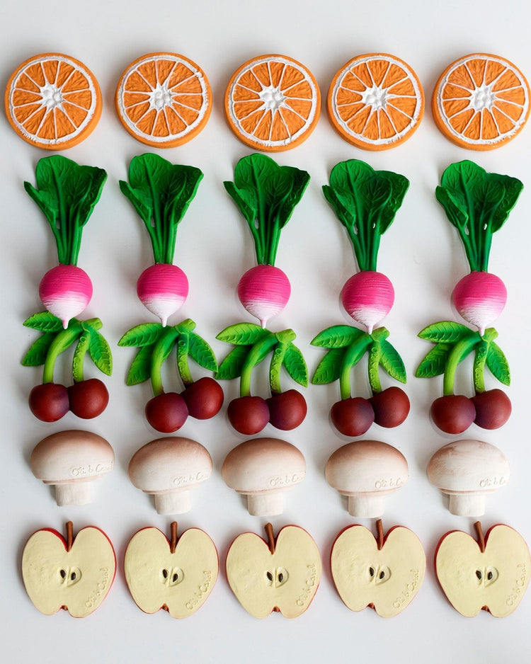 An assortment of oli + carol's mery the cherry environmentally friendly teething baby toys, designed as sliced fruits and vegetables arranged in a pattern resembling flowers on a white background.