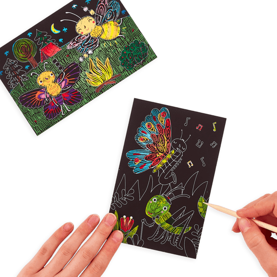 A hand holding a Ooly mini scratch & scribble art kit: bug buddies - 7 piece set with a drawing of a butterfly on it.