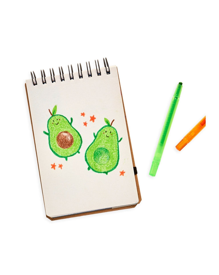 Notepad with doodles of two green avocados and stars, accompanied by Ooly yummy yummy scented twist-up crayons in green and orange.