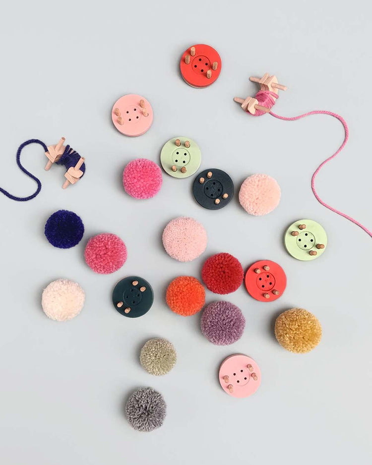 Assorted eco-friendly pom maker buttons and fabric swatches arranged on a plain surface.