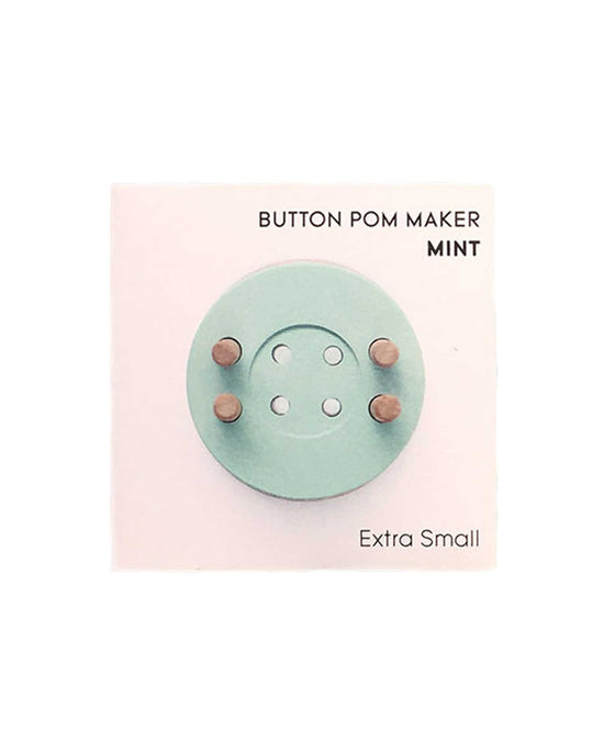 A crafty, button pom maker in mint displayed on a pale pink background.