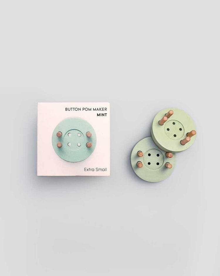A crafty button pom maker in mint color, extra small size, displayed next to its eco-friendly packaging.